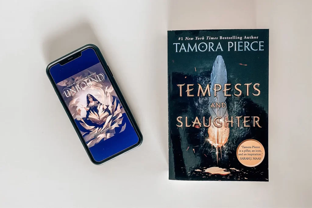 Phone with ebook Unbound cover, and Tempests and Slaughter book by Tamora Pierce.