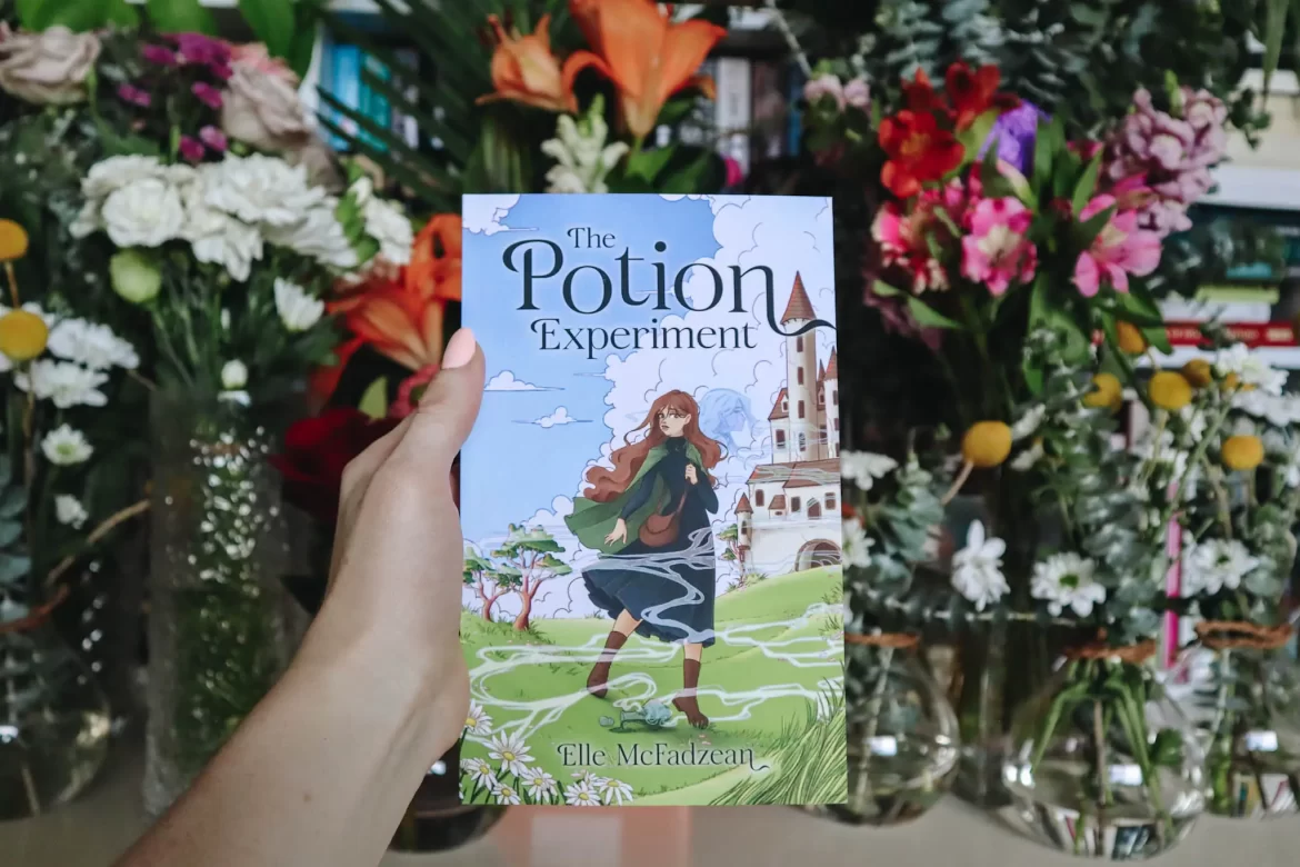 The Potion Experiment by Elle McFadzean held in front of flowers.