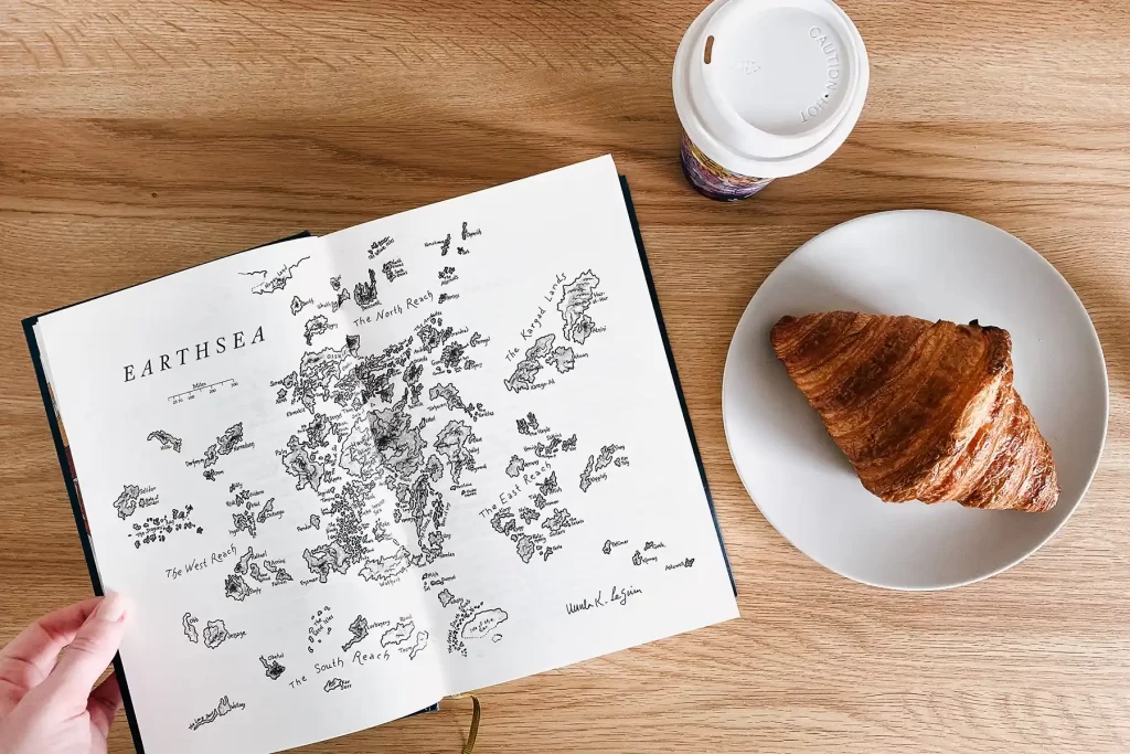 The Wizard of Earthsea map flat lay with croissant and coffee.